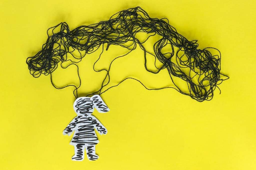 Photo for article on living with OCD intrusive thoughts. Craft collage of a paper cut out of a woman and Strings of black yarn positioned at the top of the head.