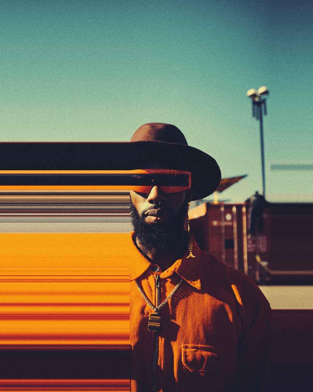 Living with treacher collins syndrome: an aged color photo of a black person with a beard and sunglasses. From the left hand of their face to the edge of the photo is distorted, symbolising the distorted view of oneself a person.