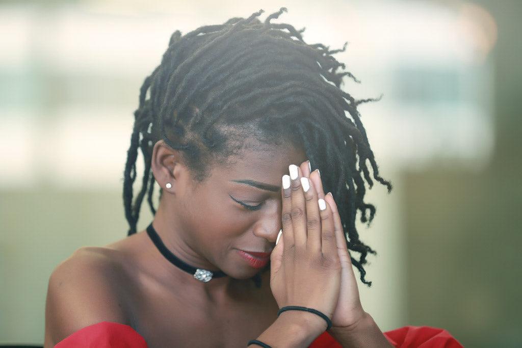Woman with closed eyes and hands pressed together beside her face.