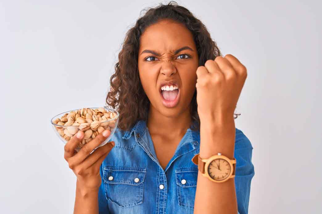 Do I Have Mast Cell Activation Syndrome? A young person is holding a bowl with pistachios standing over isolated white background looking annoyed and frustrated.