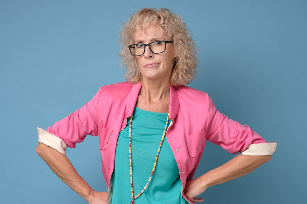 A studio photo of an older motherly tyre person thinking: 'wait until you're my age.' The women is wearing a bright pink jacket and aqua tee. 