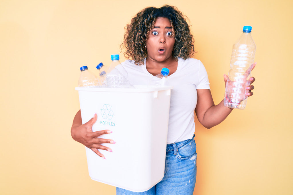 What are your pet peeves? Photo of young African American plus-size woman holding recycling wastebasket with plastic bottles scared and amazed with open mouth at seeing her partner's peeves.