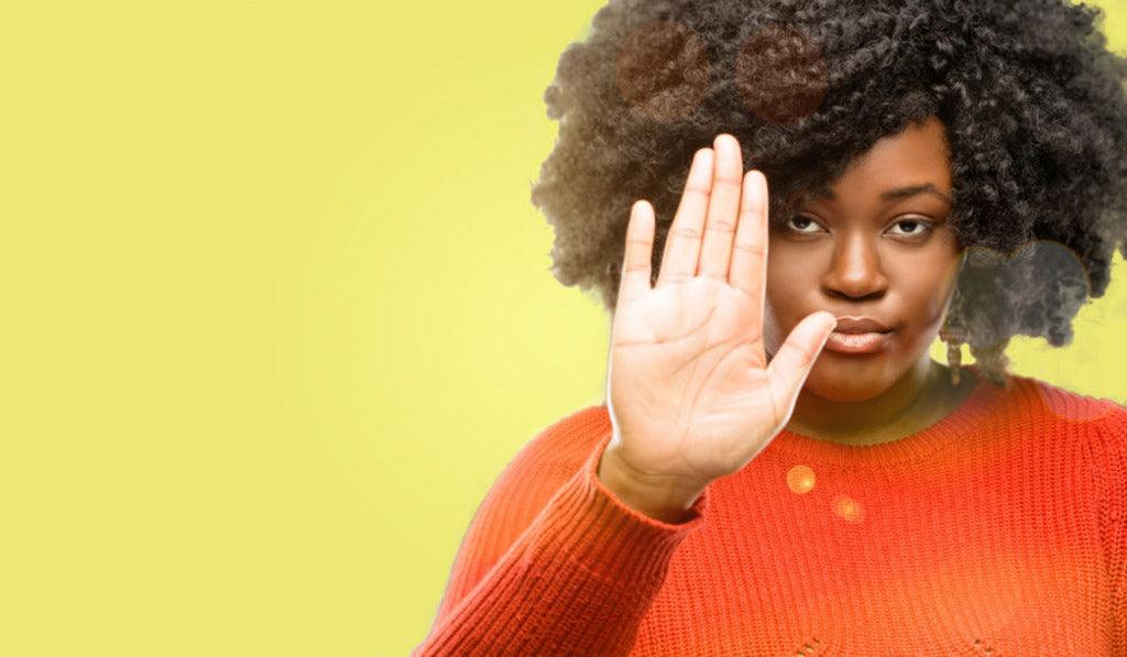 Woman in a red sweater making a stop gesture against a yellow background.