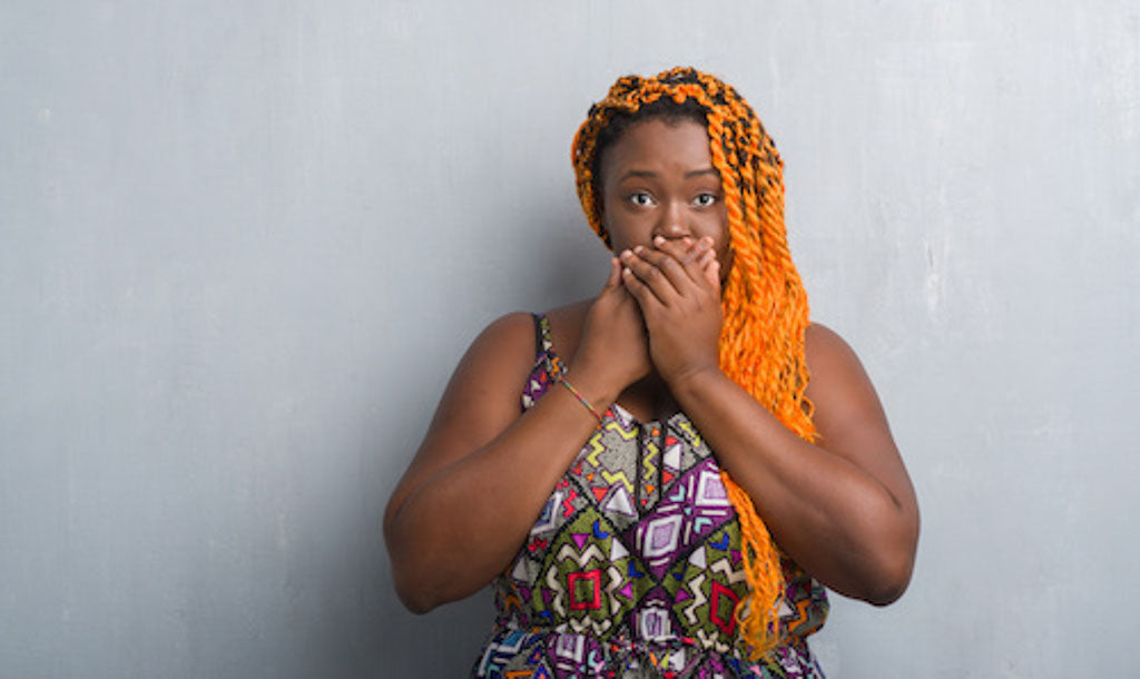 Keeping cancer a secret: a young woman looks straight on to camera with her hands covering her mouth trying to stop herself talking.