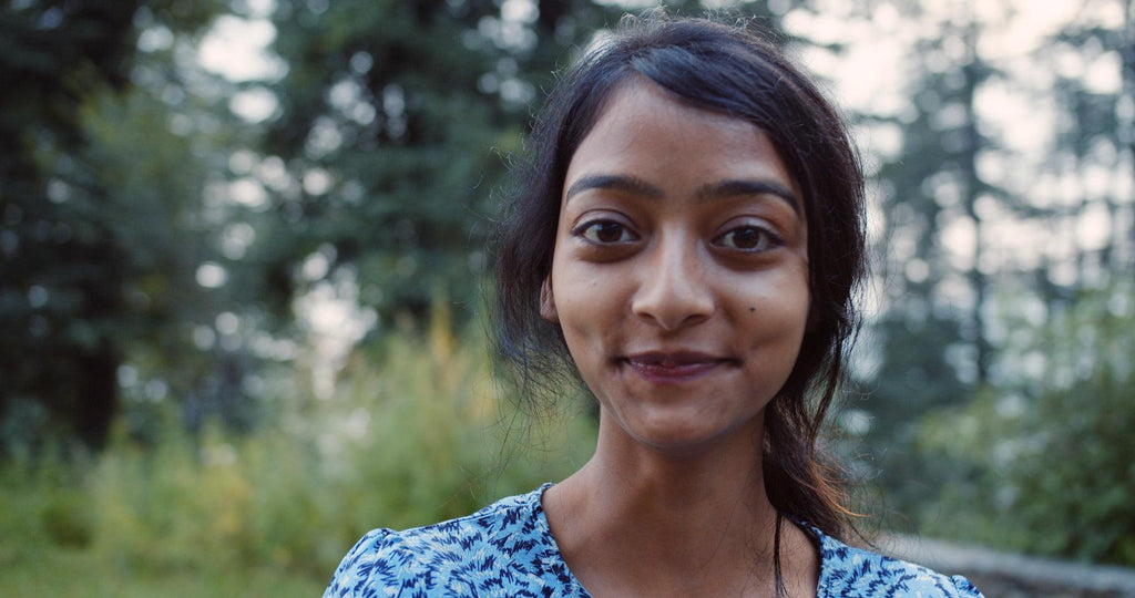 Sex and sickness: How to get my sex drive back after chronic illness: a color photo of a South Asian person standing in a forest for an article about reclaiming sex drive after chronic illness. They are smiling at the camera.