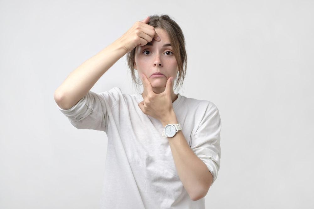 Living with kyphosis is a cause of chronic pain. This is a photo of a woman in a white long-sleeved t-shirt pulling a smile on her face. The picture conveys the concept of loss of work or being alone in pain.