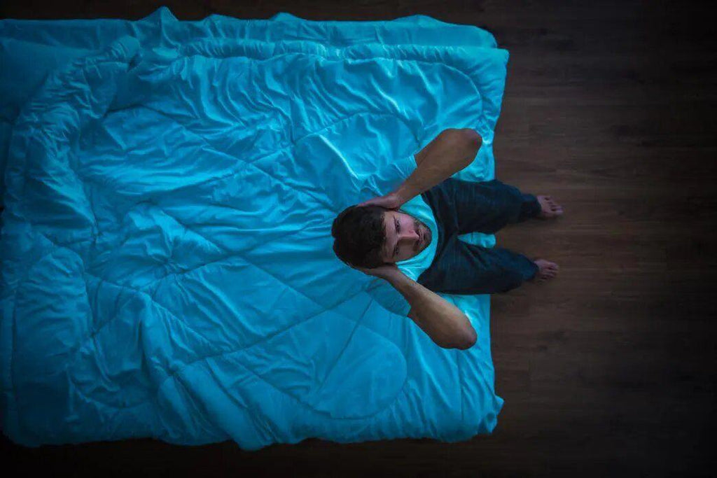 Migraines in the middle of the night:  a man is sitting on the edge of their bed covering their ears.