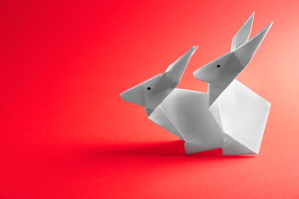 Sex after cancer therapy: origami rabbits on red color background. One on top the other, simulating sex 'doggy-style'.