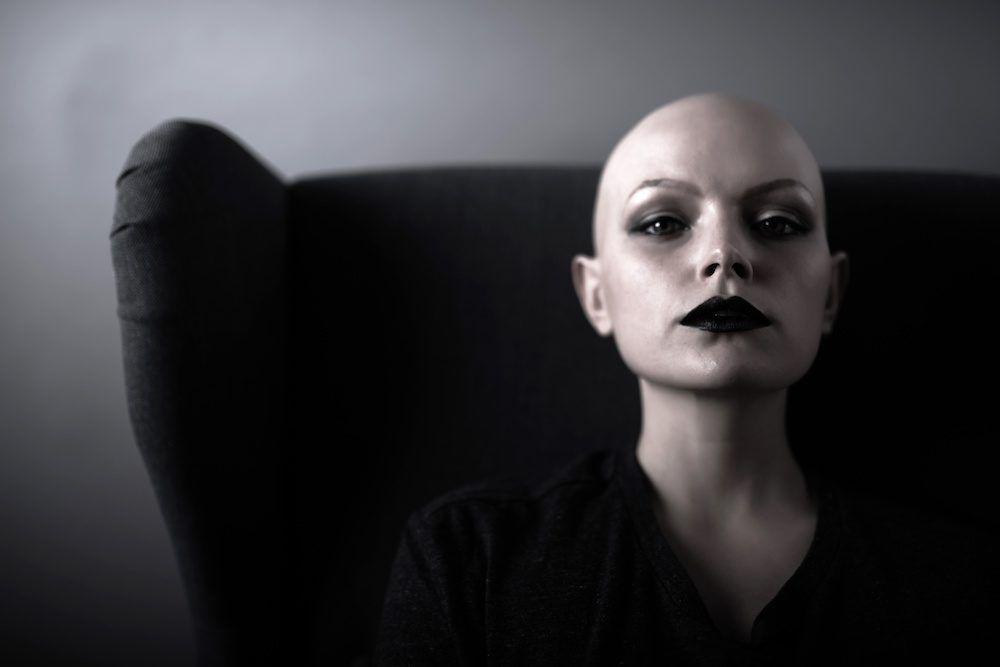 Photo for article: who qualifies as a cancer survivor? Bald woman stares defiantly at camera while seated.