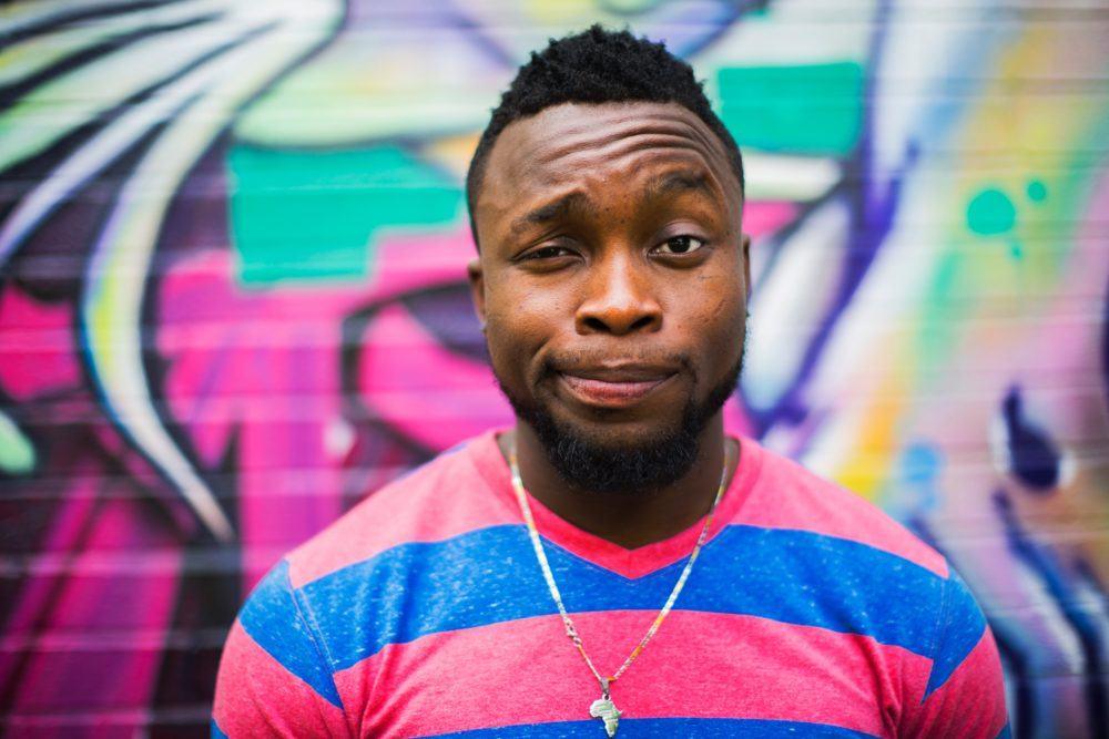 Image for article:awkward stories the one where i peed myself on a date. african american man stands before graffitied wall with slight grimace his face indicating discomfort.