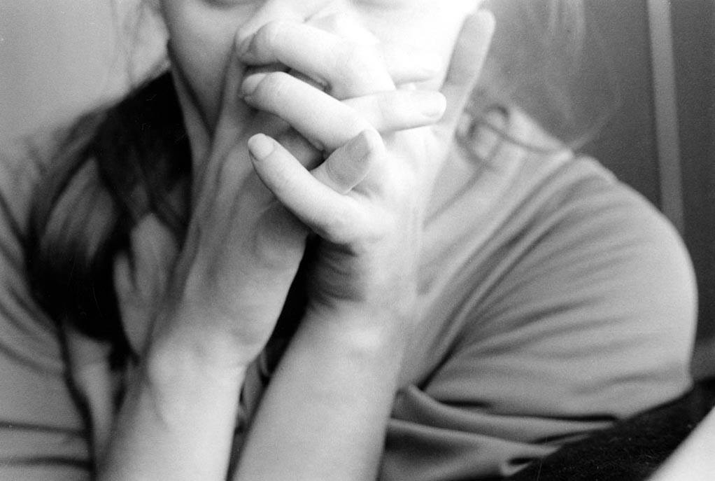 She presents well. A close up black and white photo of a person clasping their hands in front of their face. Their face is hidden in order to obscure their feelings, to maintain a facade of acceptable normality.