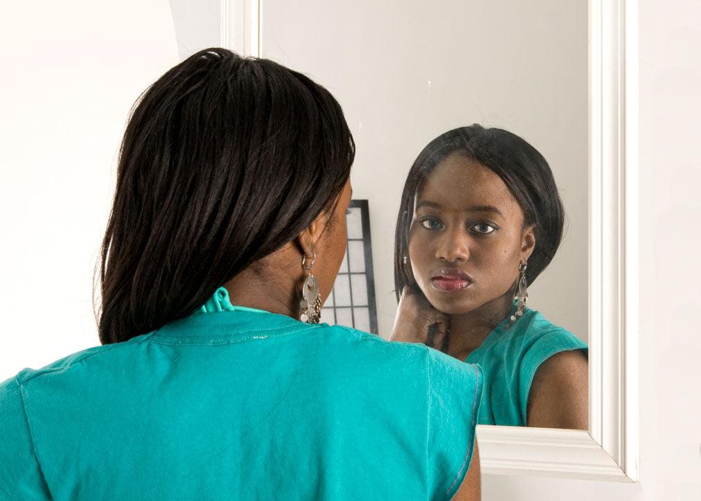 personal reflective essay: a person with long black hair, and wearing a teal dress, is having a conversation with her reflection.