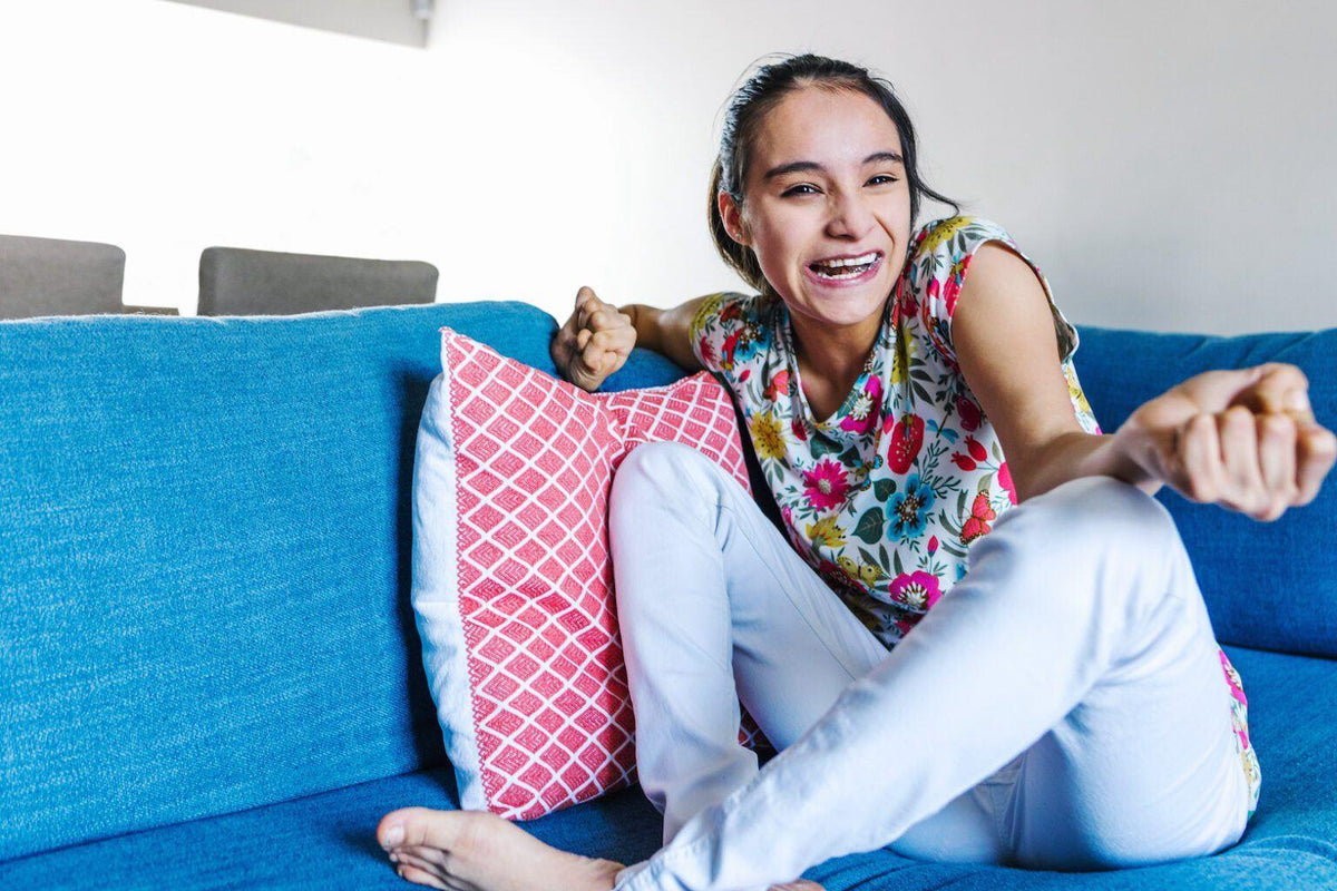 A woman sitting on a blue sofa smiles and gestures with her hands.