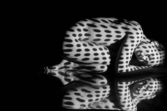 Photo for article on sex and chronic illness. Black and white photo of a naked woman hunched over. There are dots all over her body which seem to be coming from a light reflection.