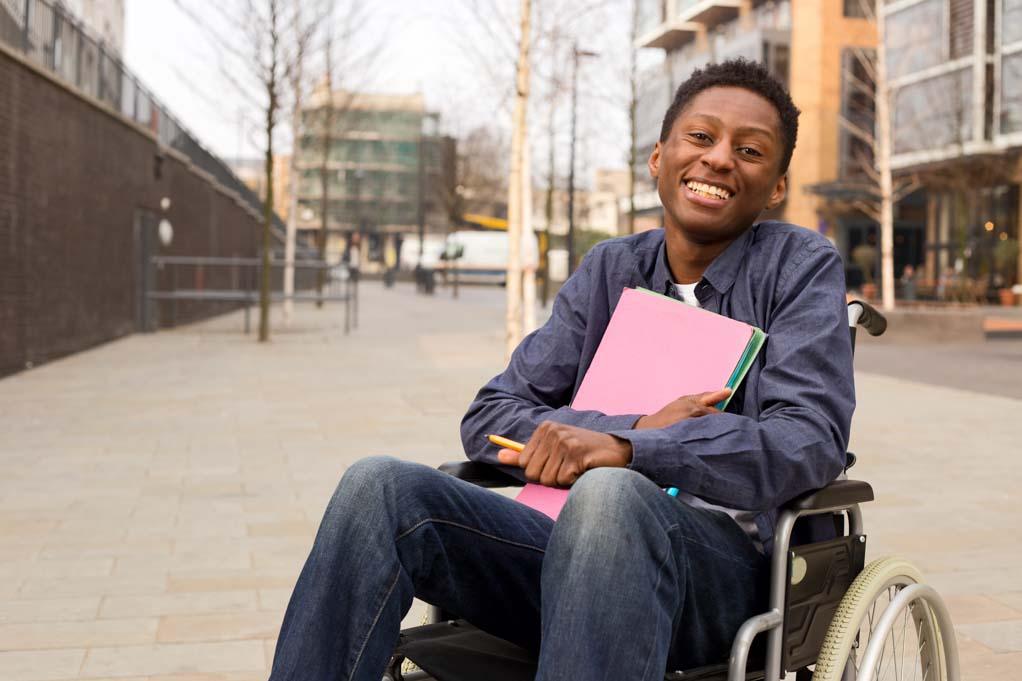 Image for an article on inclusive job descriptions: a happy young disabled man in a wheelchair holding folders after securing a new job.