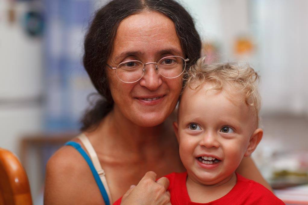 An adult wearing glasses holds a smiling child indoors.
