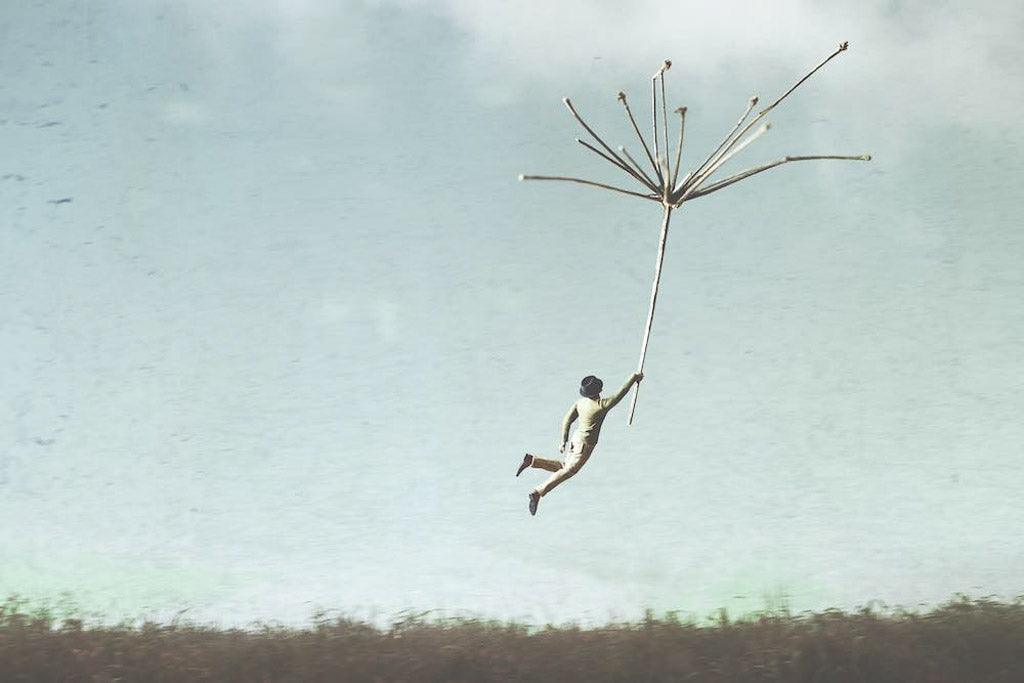 When someone you love has an addiction: surreal image of a person with a black top hat being pulled up into a cloudy sky by a dandelion.