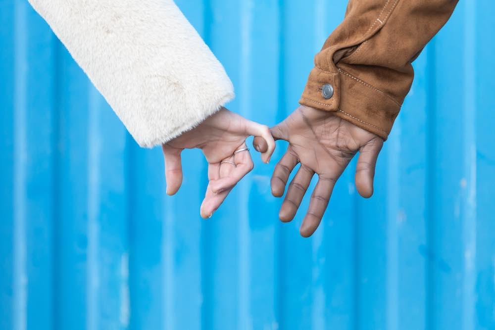 The healing benefits of human touch help ease pain. Closeup shot of interracial couple's hands touching in front of a blue metal wall.
