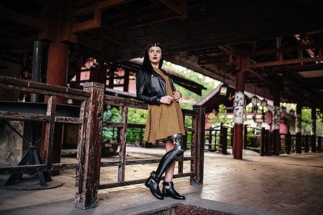 Disabled models: a stunning woman poses in what looks like an old building of Chinese history, but there aren't many inside details, so we can't be sure. She is wearing a mustard dress with a chic black leather jacket over it.