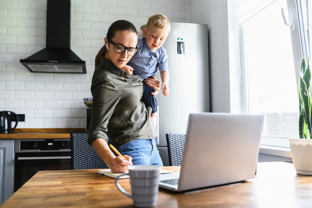 A busy mom works at home with an active toddler on her arms.