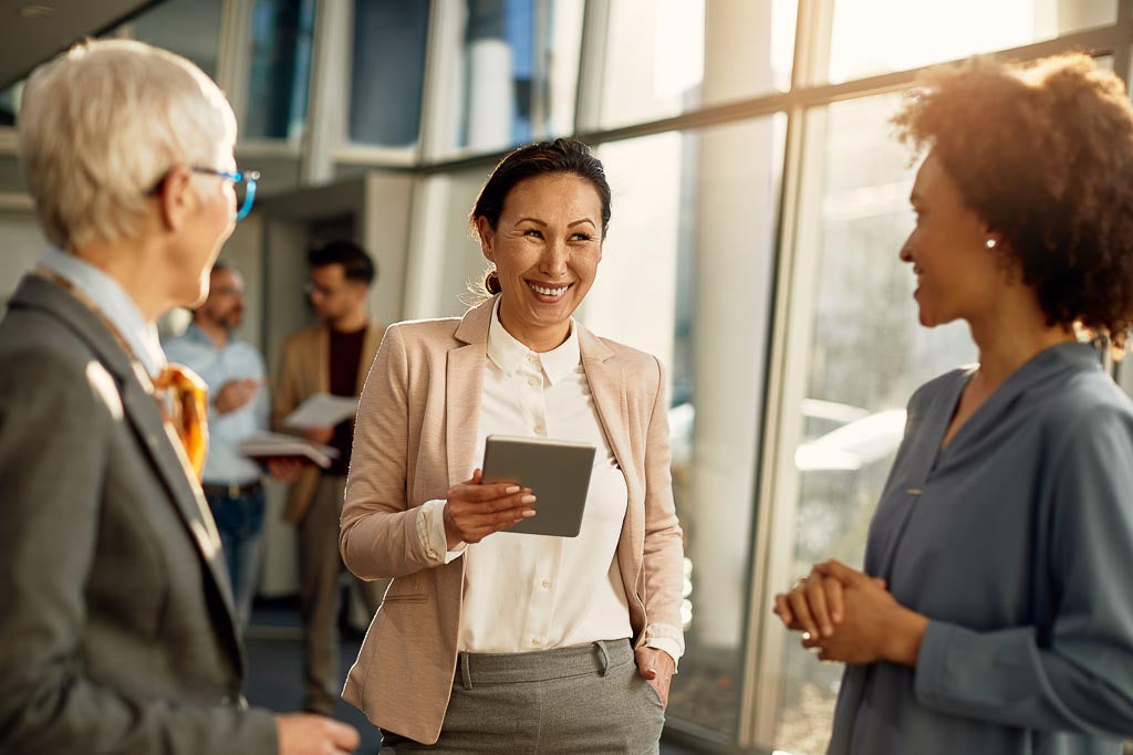 Improve mental health at work by communicating with colleagues: a female CEO is smiling while talking to two female employees while holding an iPad.