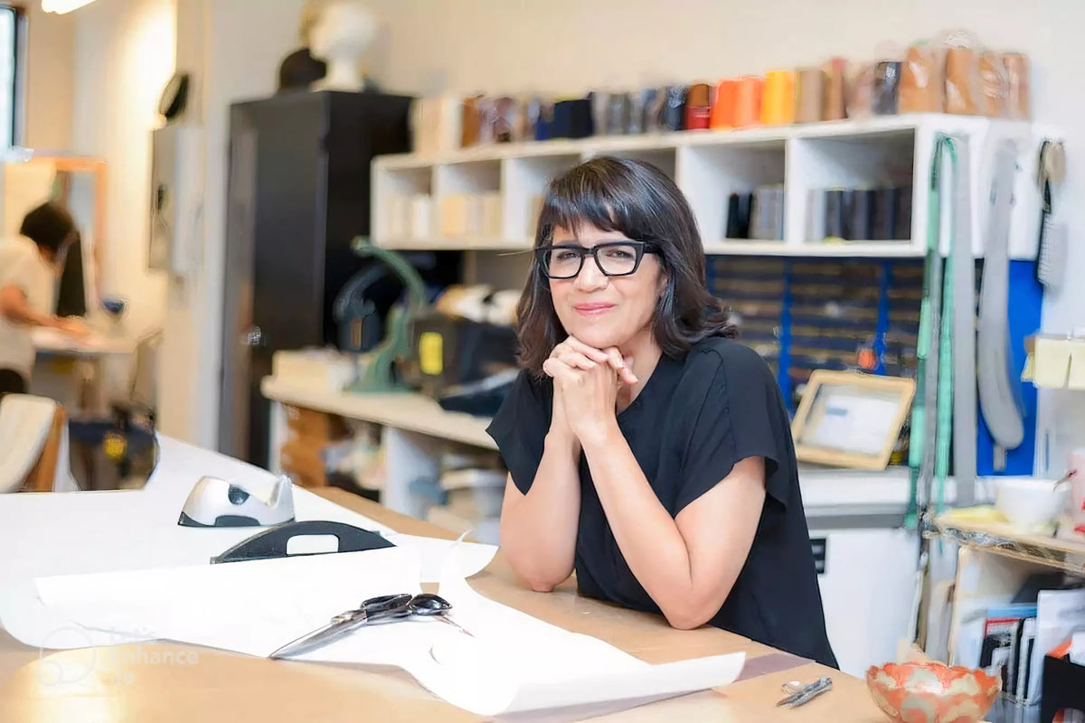 Izzy Camilleri, designer of IZ Adaptive Clothing, sitting in her fashion studio with sewing materials and tools in the background.