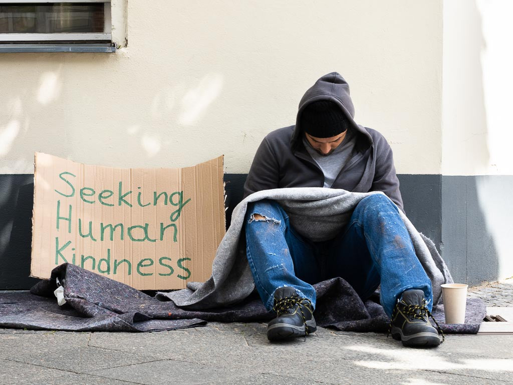 Mean things said about homeless people: photo a homeless person with a cardboard sign "seeking human kindness."