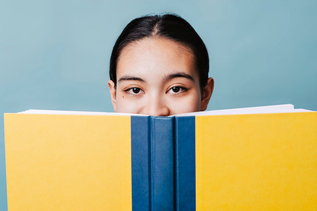 Misconceptions about dyslexia: a young teenager smiles behind a yellow book while smiling.