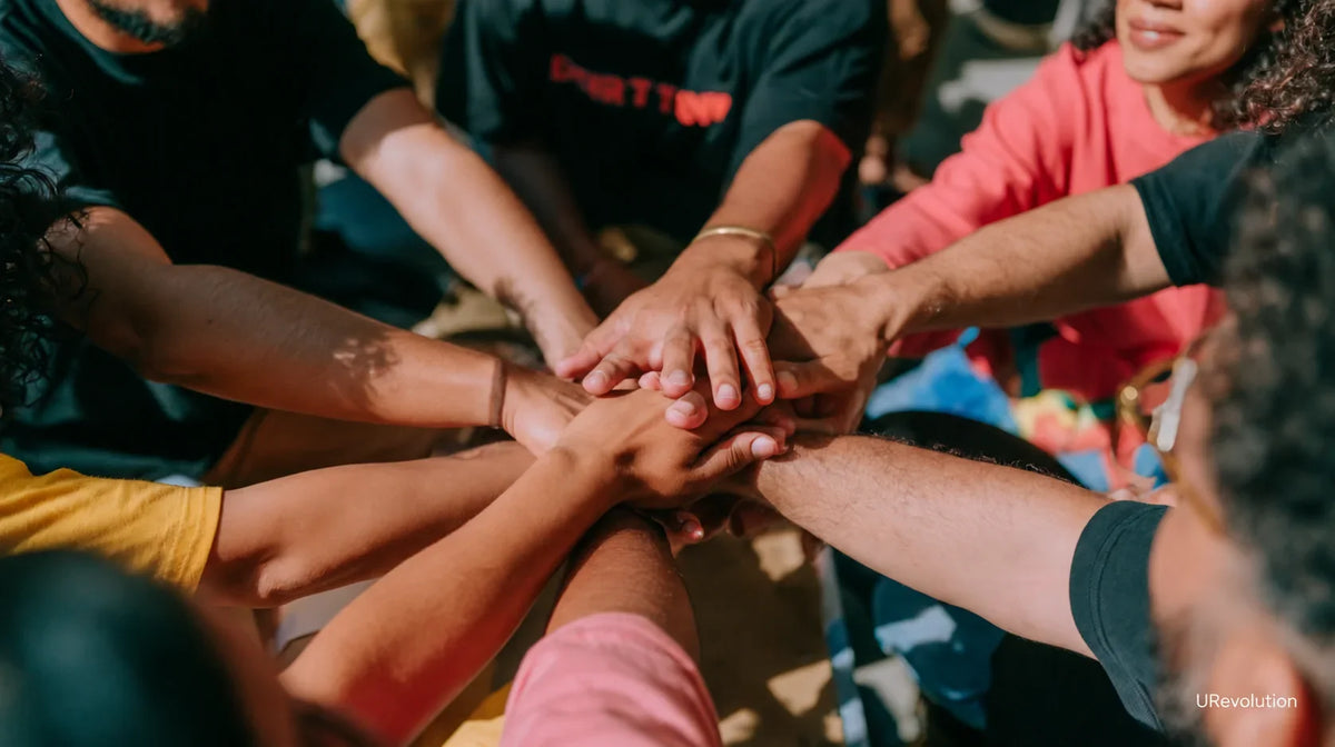 People of different skin tones stack their hands together in a circle.