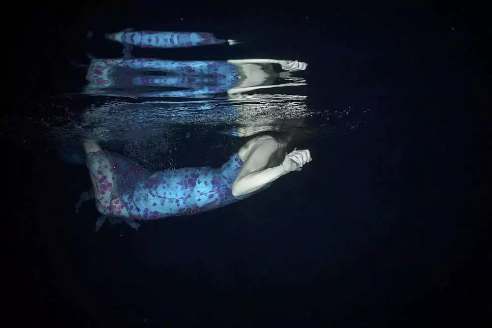 A person in a patterned dress underwater, reflected in the surface above.