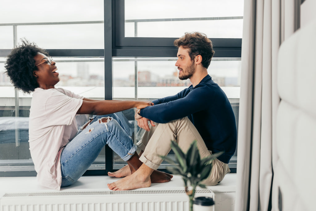 Reclaim your wellbeing: photo of a happy interracial couple looking at the window of their newly rented house, sitting in empty room. 