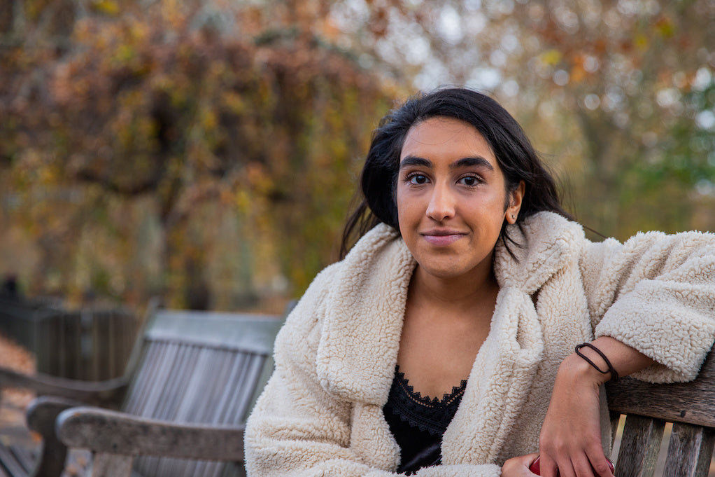 A young Indian woman, who has had a recovery from a nervous breakdown, sits on a public bench, offering a shy smile towards the camera.