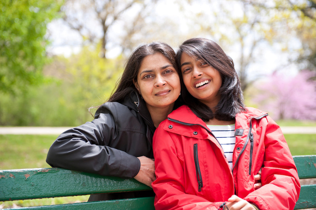Reducing the stigma of mental illness: a mother and daughter sit on a park bench in spring smiling at the camera.