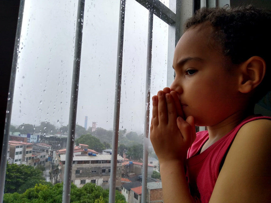 A child with scrupulosity OCD is praying at a window when it is raining outside.