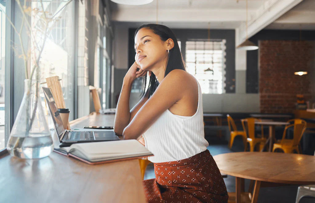 A woman stands by a window, leaning on a bench, reflecting on starting a mental health blog.