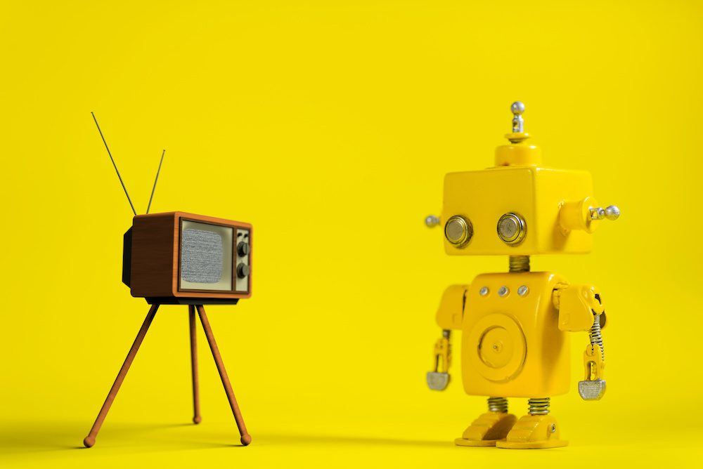 Photo for article on toys for disabled children. Yellow handmade robot on a yellow background staring at a retro television set.