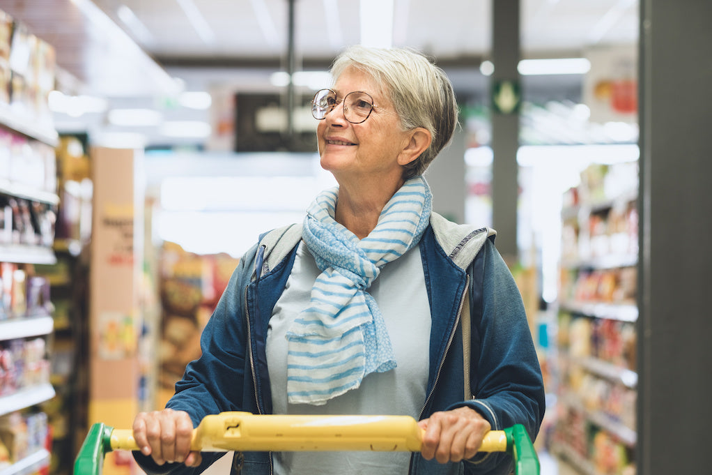 A woman, shopping with rheumatoid arthritis, is smiling as she pushes a trolley in a supermarket.