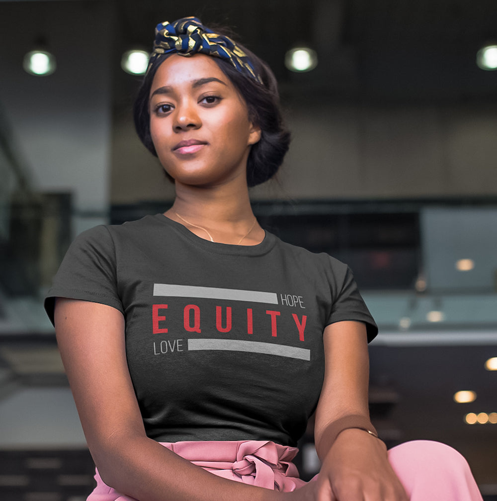 A Black woman is wearing a dark gray t-shirt with the words Hope Equity Love printed on it.