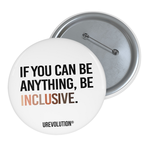 A photo of a 3" white Be Inclusive Racial Diversity pin button promoting an end to racism. On the front of the pin button is the phrase: "If you can be anything, be inclusive," in black upper case letters. The text is all black, except the word "Inclusive," which is in different skin colors, with the lightest color on the left and the darkest on the right. 