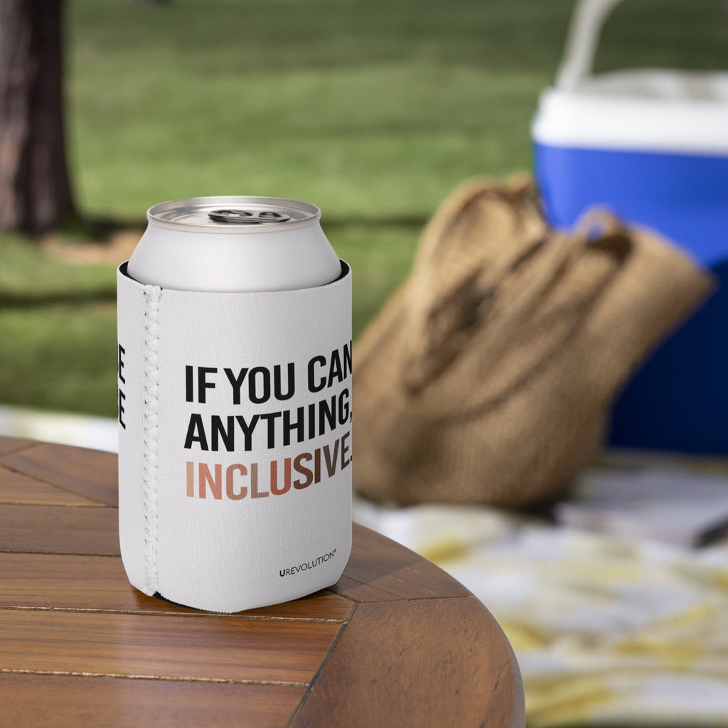 A 12 oz Inclusive Diversity Koozie is on a picnic table. On the front of the neoprene diversity koozie, in upper-case letters printed on a white koozie, is the phrase, "If you can be anything, be inclusive." The text is all black except for the word "Inclusive," which is in different skin colors, with the lightest color on the left and the darkest on the right promoting racial equality.