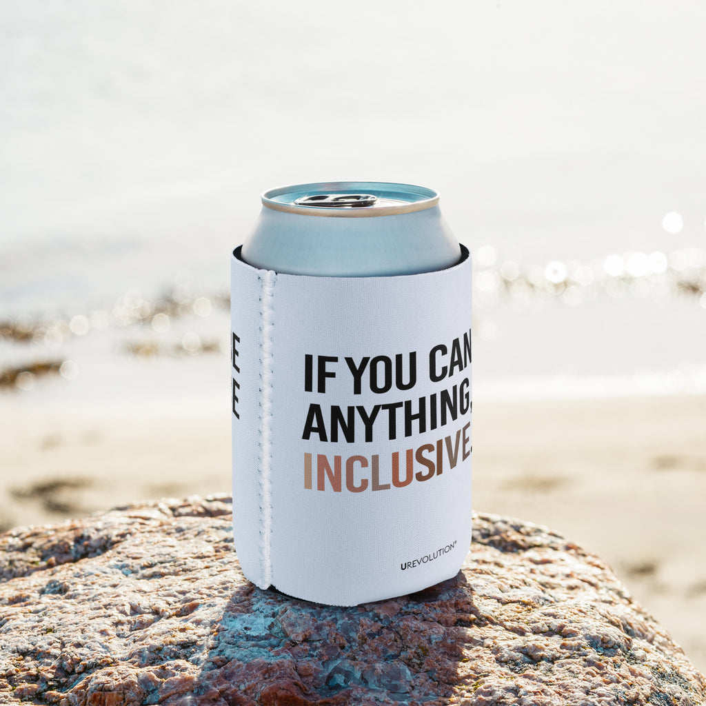 A 12 oz Inclusive Diversity Koozie is on a rock at the beach. On the front of the neoprene diversity koozie, in upper-case letters printed on a white koozie, is the phrase, "If you can be anything, be inclusive." The text is all black except for the word "Inclusive," which is in different skin colors, with the lightest color on the left and the darkest on the right promoting racial equality.