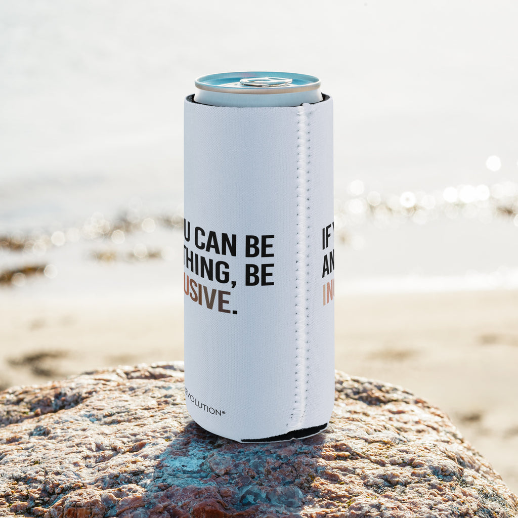A slim 12 oz Inclusive Diversity Koozie. On the front of the neoprene diversity koozie, in upper-case letters printed on a white koozie, is the phrase, "If you can be anything, be inclusive." The text is all black except for the word "Inclusive," which is in different skin colors, with the lightest color on the left and the darkest on the right promoting racial equality. The koozie is shown at the beach on a rock.