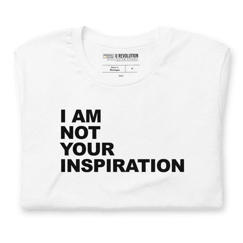 This is a white 'I Am Not Your Inspiration" t-shirt. On the top third of the inspiration shirt is the phrase, "I am not your inspiration," printed over four lines in black upper case letters. The tee is neatly folded.