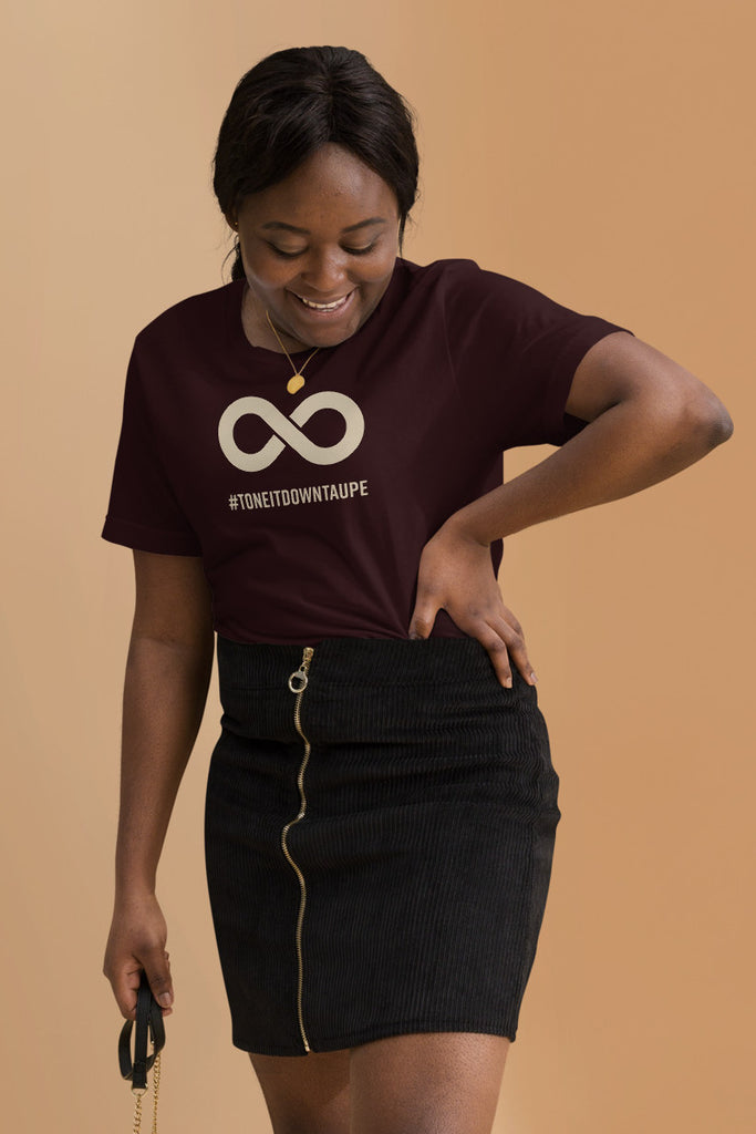 This is a photo of a woman wearing an oxblood black Tone It Down Taupe shirt. In the middle top one-third of the tee is a taupe colored infinity symbol. Beneath the symbol is the hashtag word printed in bold upper case letters: #ToneItDownTaupe