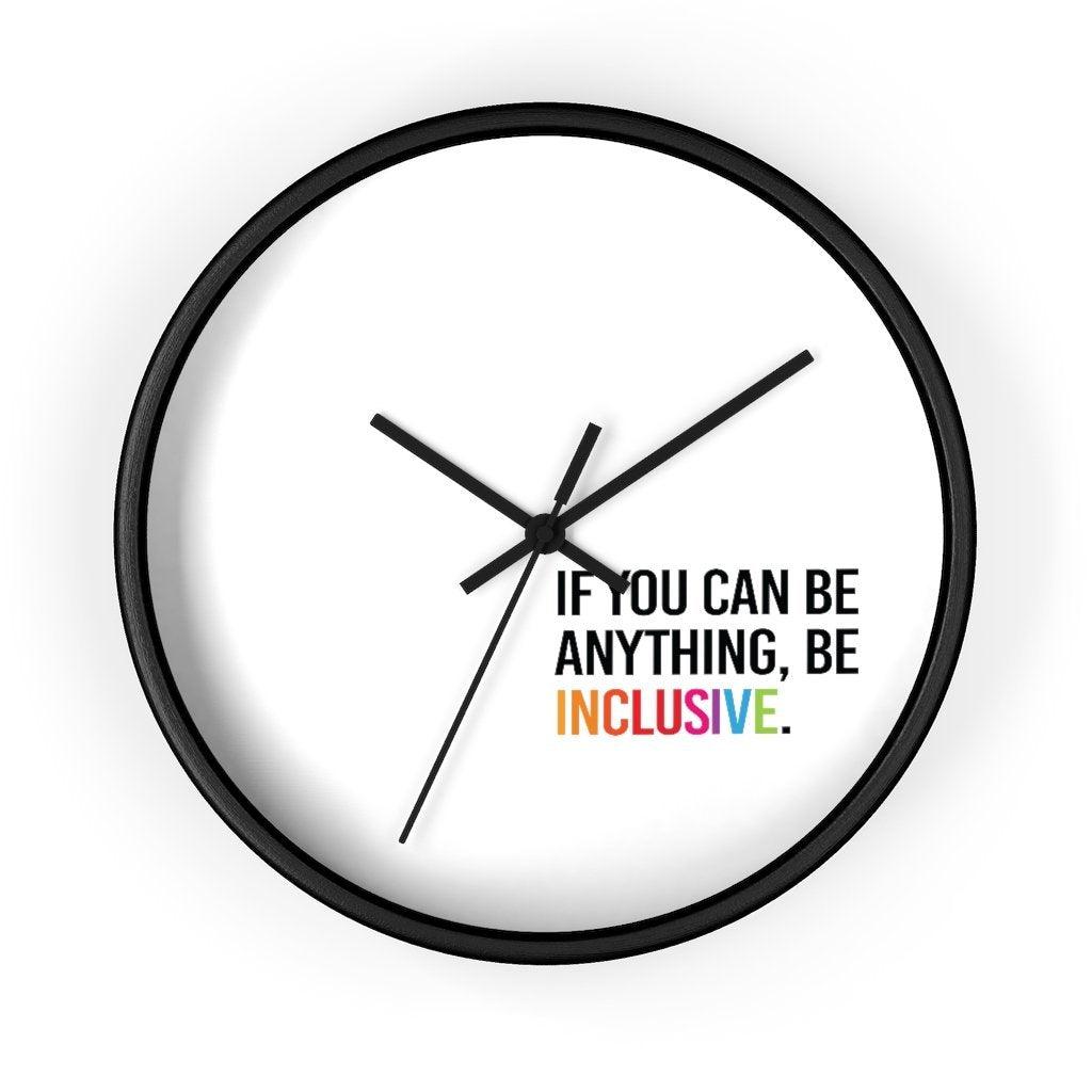 The clock has a black wooden frame and a white face. The hands are black and there are no numbers. In the bottom white quadrant of the clock face is text printed in all caps: "IF YOU CAN BE ANYTHING, BE INCLUSIVE." All text in black, except "Inclusive" which is in rainbow colors.
