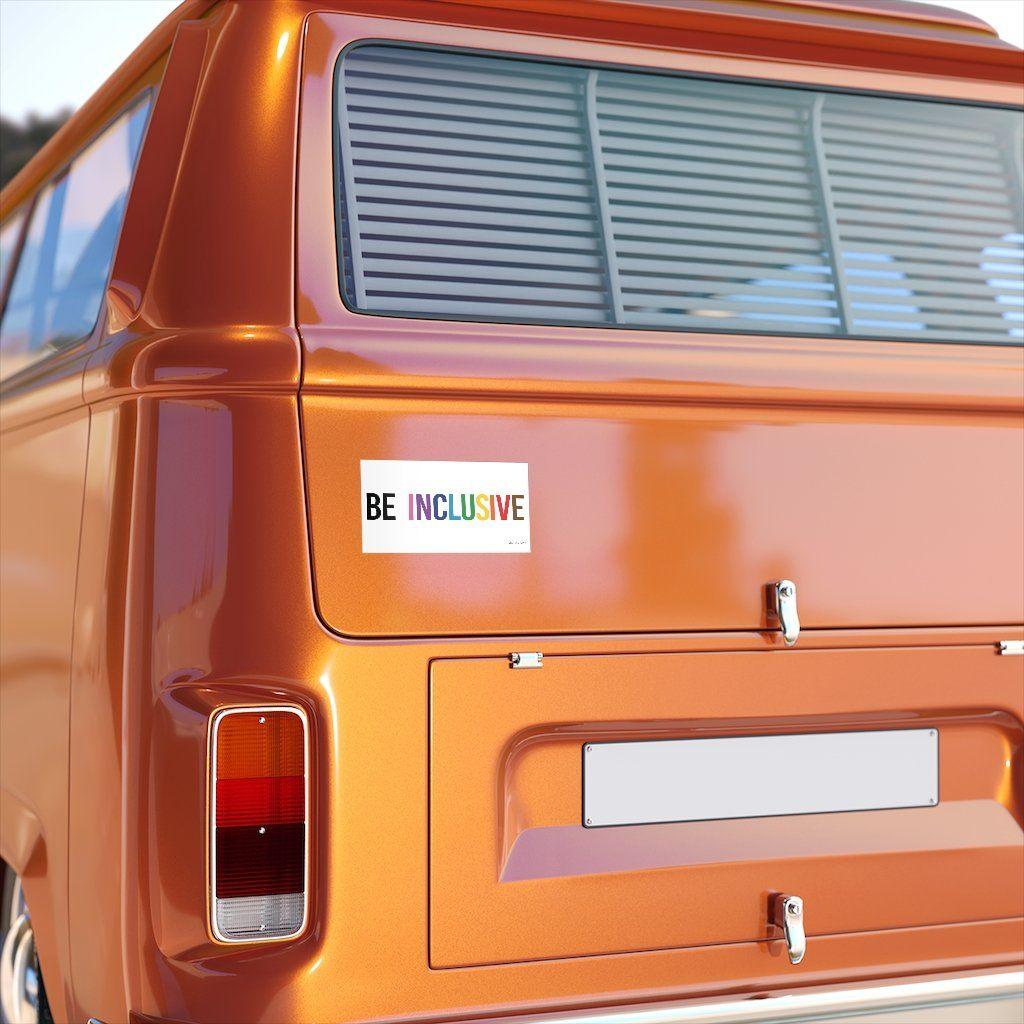 A photo of an inclusion bumper sticker on the rear of an orange camper van. The words "Be Inclusive" are printed on a white background in upper case letters. The word "be" is in black, with word "inclusive" is in the colors of the rainbow. In small upper case letters, in the bottom corner of the sticker, is the word URevolution