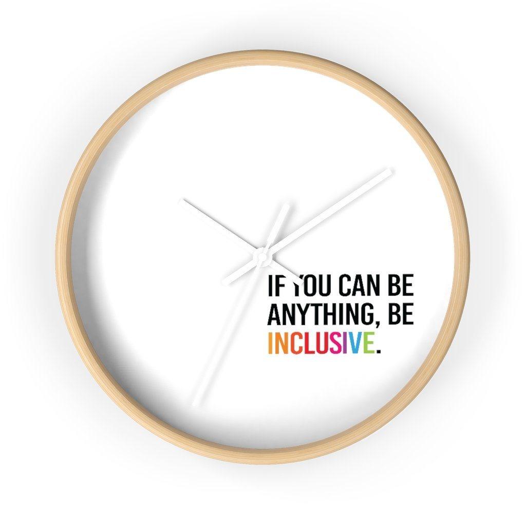 The clock has a light wooden frame and a white background. The hands are white and there are no numbers. In the bottom white quadrant of the clock face is text printed in all caps: "IF YOU CAN BE ANYTHING, BE INCLUSIVE." All text in black, except "Inclusive" which is in rainbow colors.
