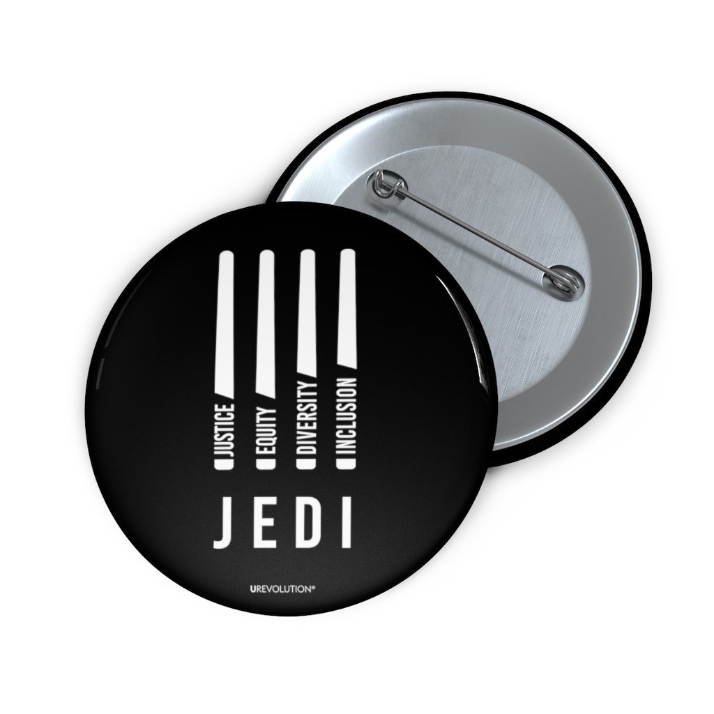 A photo of a JEDI pin by URevolution. In the middle of the black JEDI pin are four white lightsabers. At the bottom of each saber representing the saber handle is one word: Justice Equity Diversity Inclusion. Beneath the sabers is the acronym JEDI.