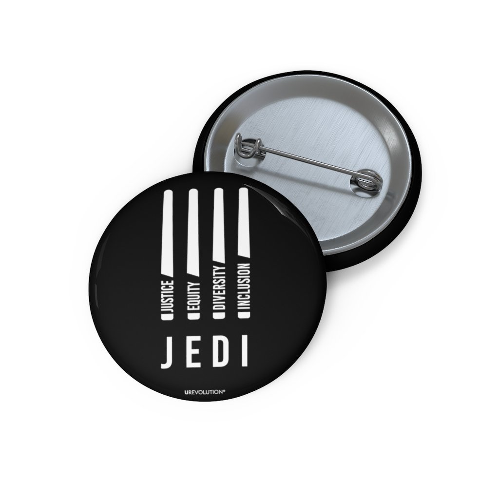 A photo of a JEDI pin by URevolution. In the middle of the black JEDI pin are four white lightsabers. At the bottom of each saber representing the saber handle is one word: Justice Equity Diversity Inclusion. Beneath the sabers is the acronym JEDI.
