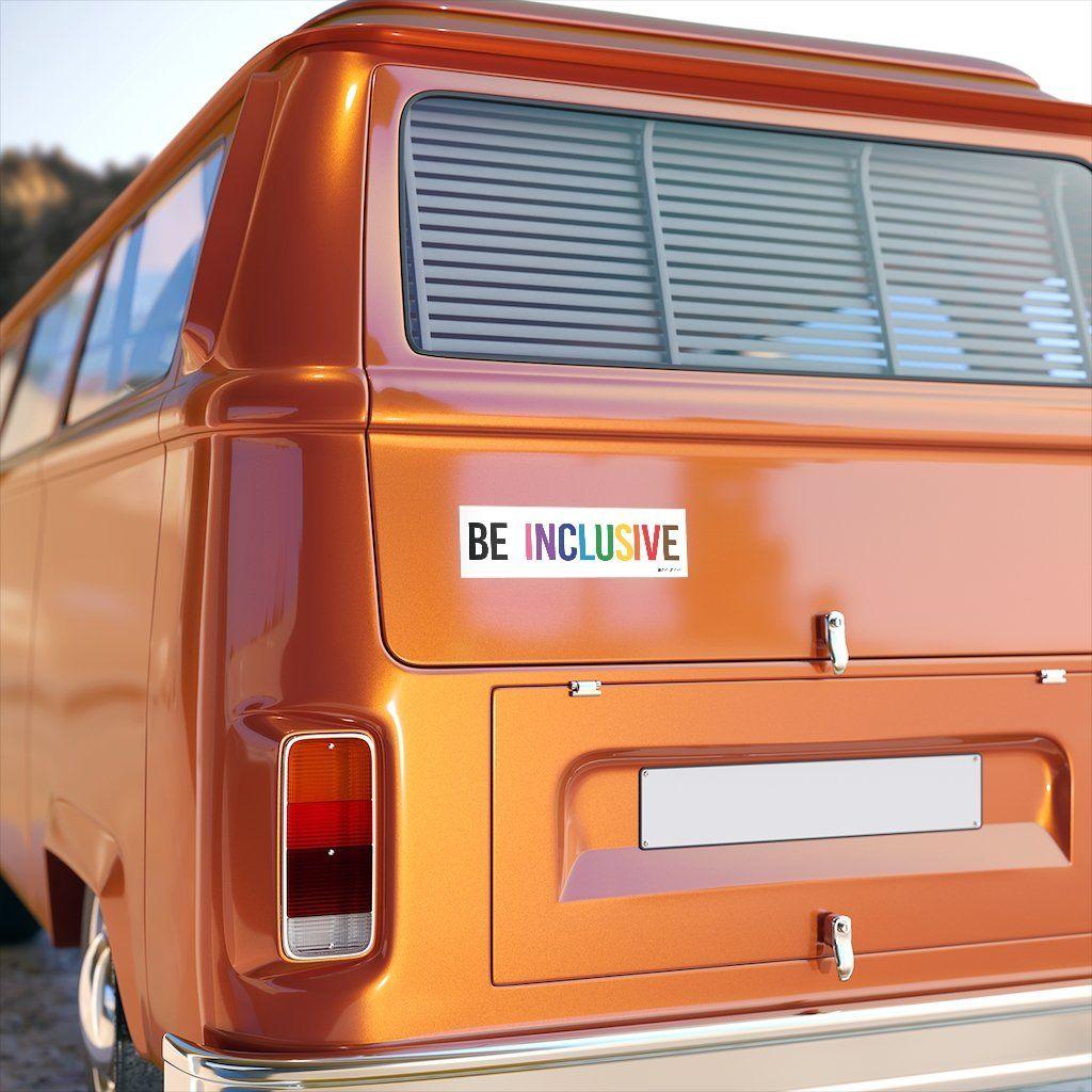 A photo of an inclusive bumper sticker on the rear of an orange camper van. The words "Be Inclusive" are printed on a white background in upper case letters. The word "be" is in black, with the word "inclusive" in the colors of the rainbow. In small upper case letters, in the bottom corner of the sticker, is the word URevolution.